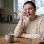 Femme adulte avec une conjonctivite hivernale qui tamponne son œil rouge irrité avec un mouchoir à la maison